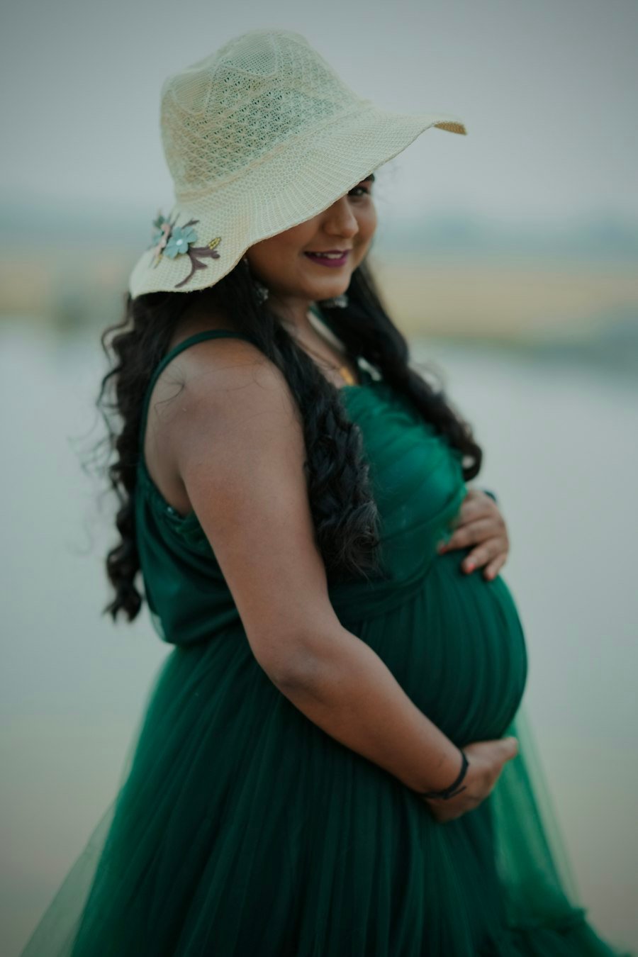 A smiling mother-to-be in a green dress holding her baby bump